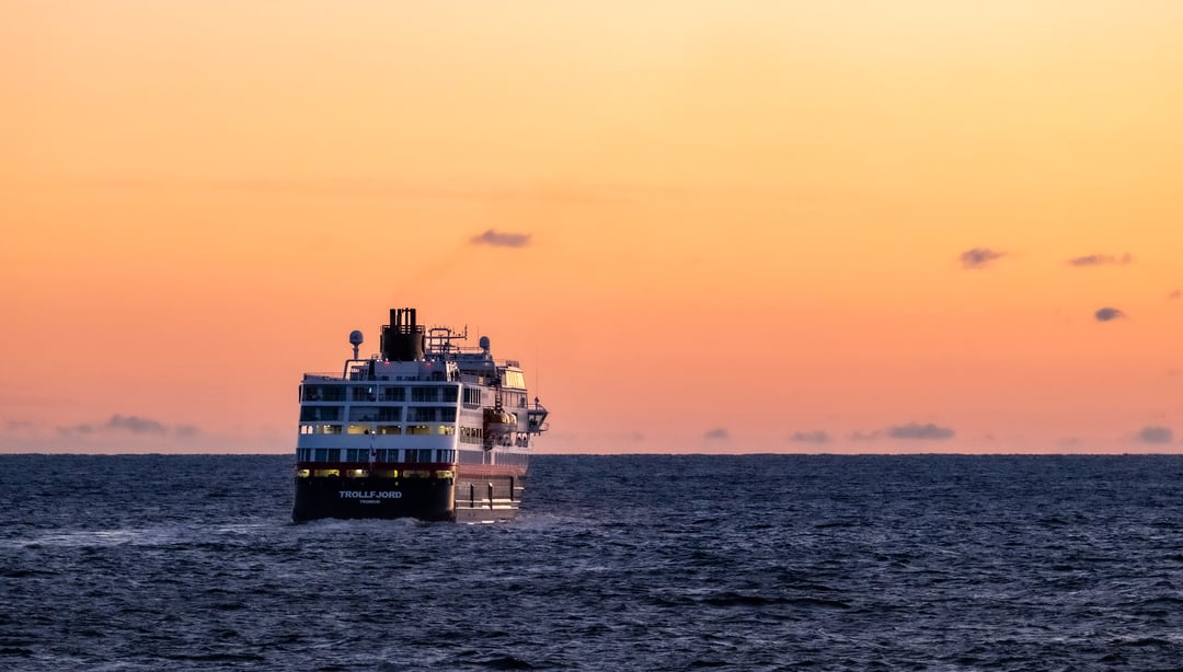 MS Trollfjord seiler ut i horisonten, i solnedgang.