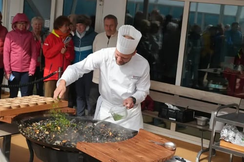 chef is actively engaged in cooking, stirring a sizzling pan filled with what appears to be a mix of vegetables and possibly meat. The chef is dressed in an all-white uniform, complete with a hat, indicating a professional cooking environment.