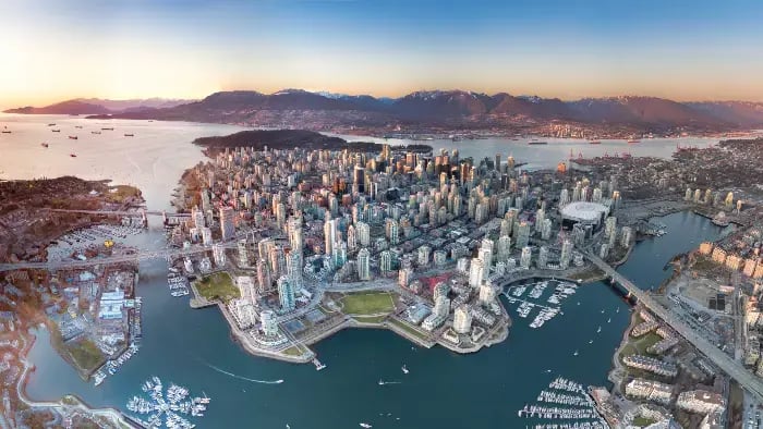 Et panormaisk dronebilde av Vancouver sentrum - mange skyskrapere, og sentrum er omringet av vann på 3 kanter.