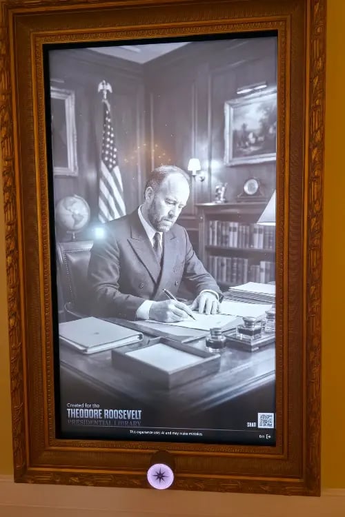 a framed picture screen displaying a black and white photograph of Theodore Roosevelt looka like in a study room setting.