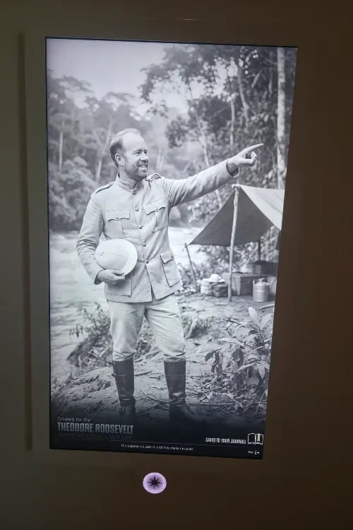 a vintage black and white photograph of a historical figure in military attire, pointing outdoors with a tent and forest background.
