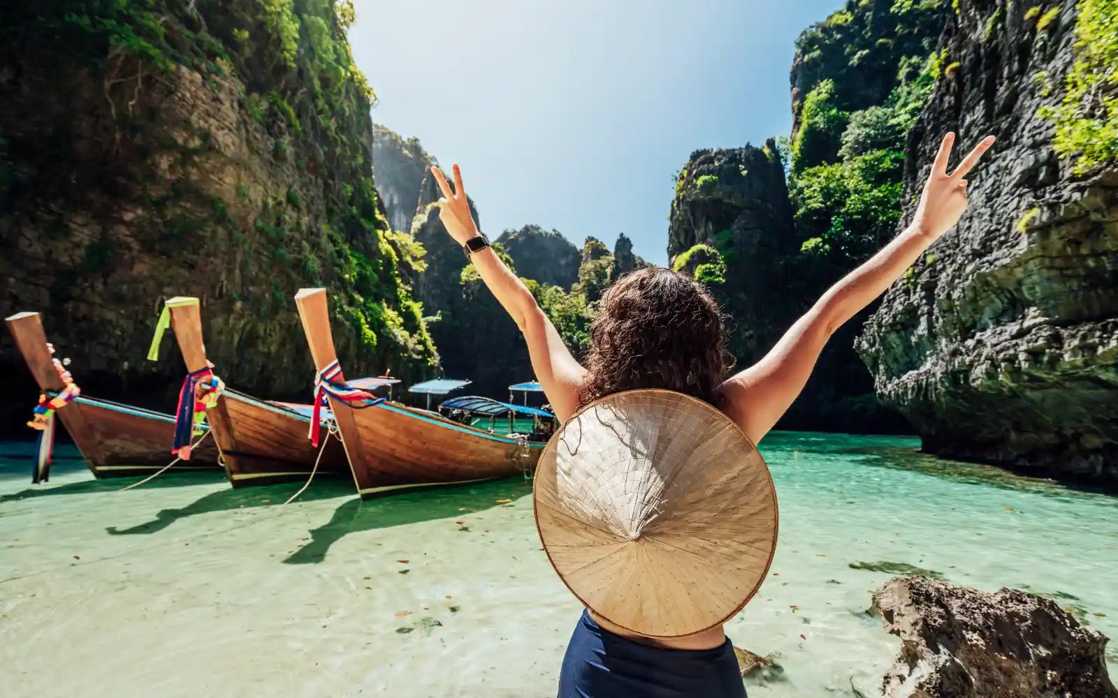 En kvinne som strekker hendene i været, endelig fremme på en strand i thailand.