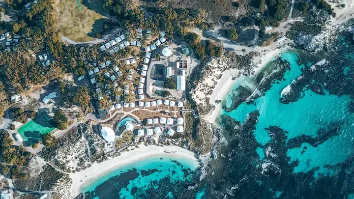 Flyfoto av Discovery Rottnest Island med telt mellom buskene og en turkis bukt ved siden av.
