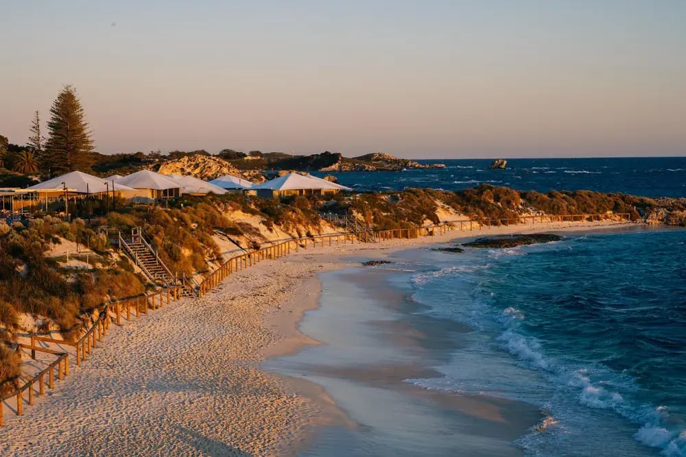 Strand i solnedgangslys med hvite solseil og telt oppe i sanddynene.