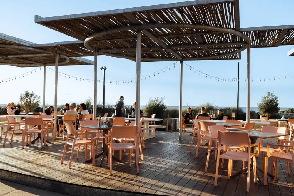 Restaurantterrasse med gjester under et skyggetak av tre.