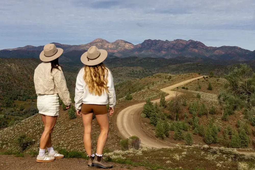 To kvinner med hatter ser utover en slynget vei og fjellene i Flinders Ranges.
