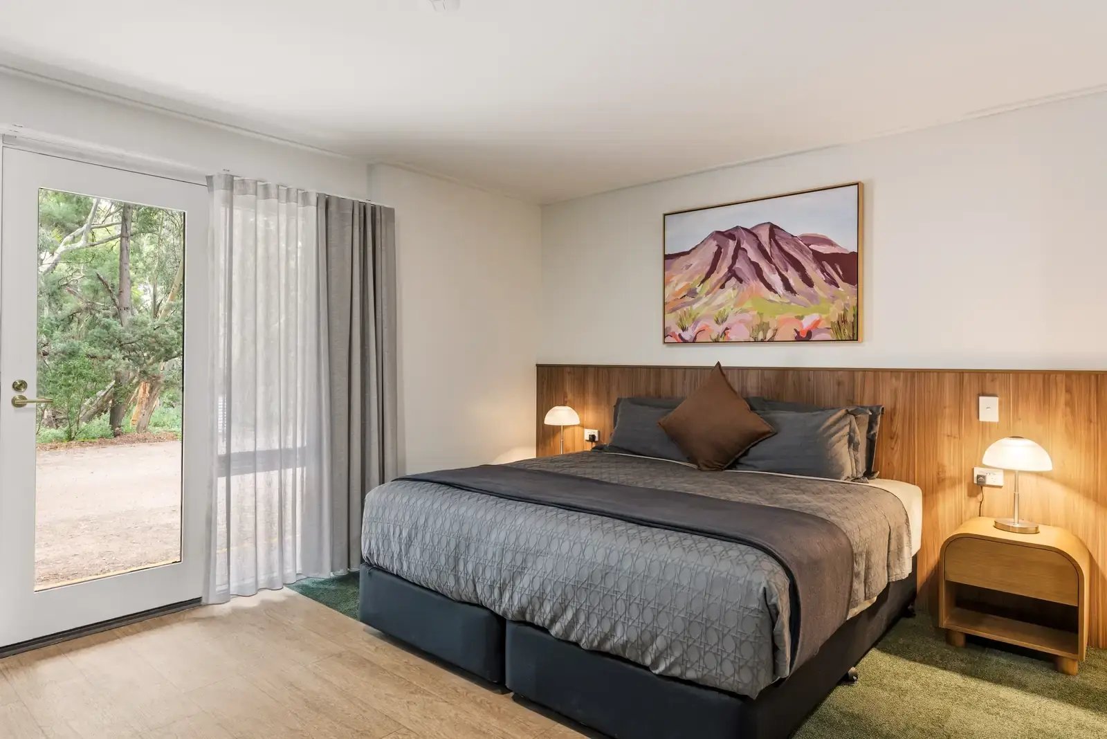 Hotellrom med dobbeltseng, trepanel og maleri av et fjell på veggen.