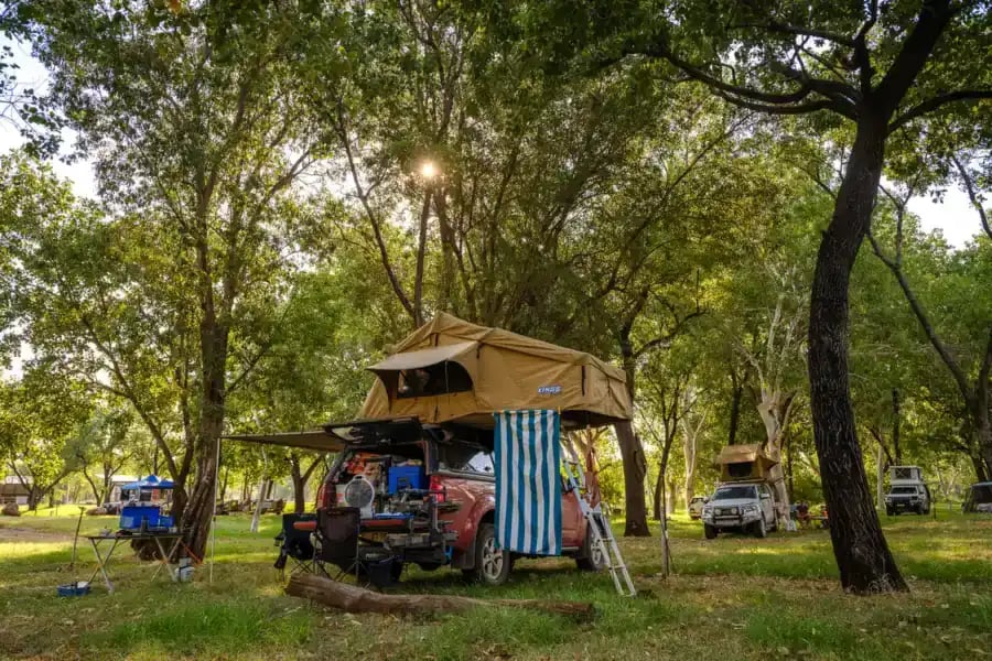 Bil med teltoppsett på plenen under trær på campingplassen.