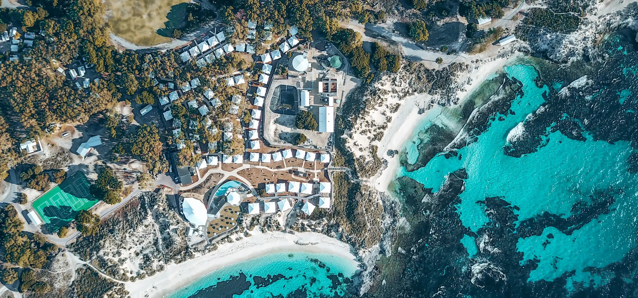 Flyfoto av Discovery Rottnest Island med telt mellom buskene og en turkis bukt ved siden av.