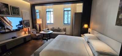 Romslig rom på Capell Sydney. Stor dobbeltseng, sittegruppe med sofa, bord og stol og tv og bilder hengende på veggen.