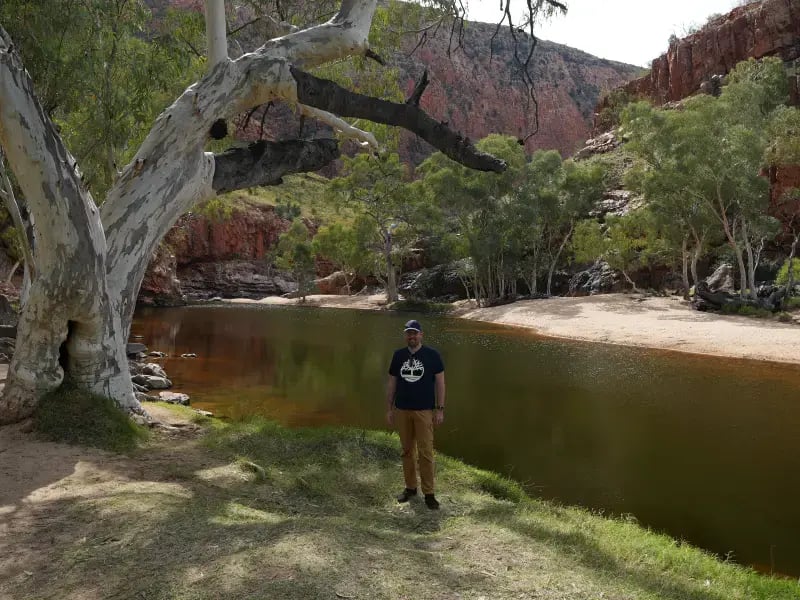 A person stands on the bank of a river surrounded by natural scenery.
