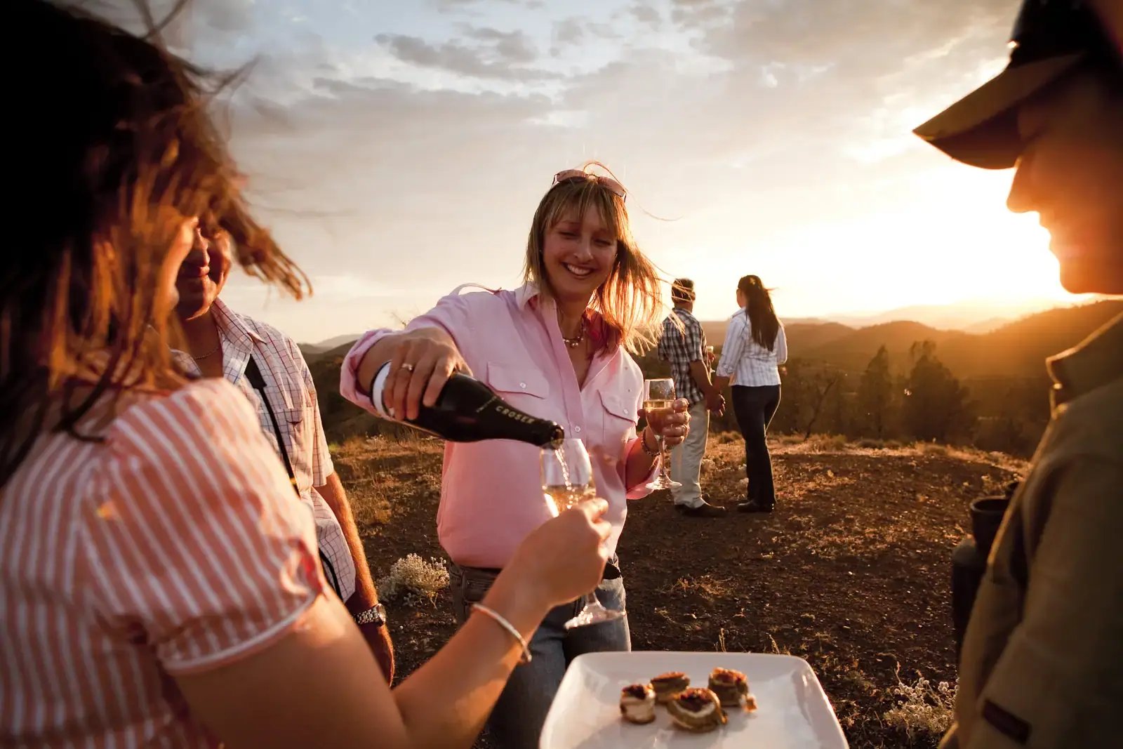 Gjester skjenker musserende vin i solnedgangen.