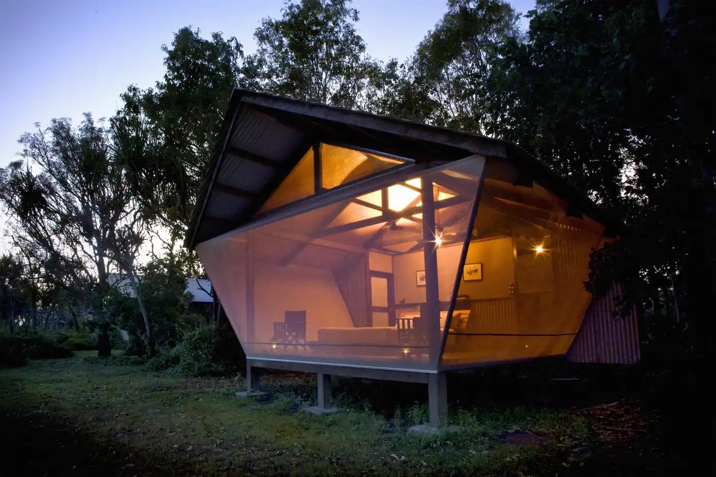 Safaribungalow med glassvegg som lyser i skumringen.