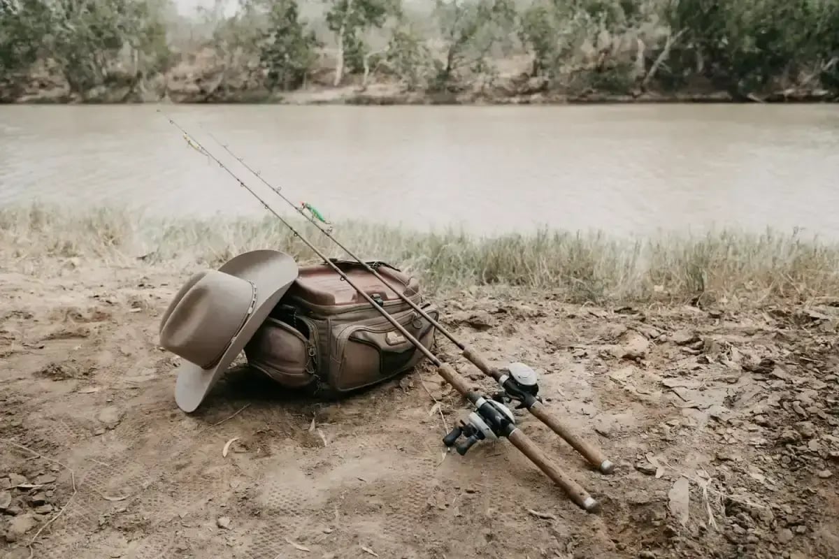 Fiskestenger, lærveske og cowboyhatt på elvebredden ved Bullo River.