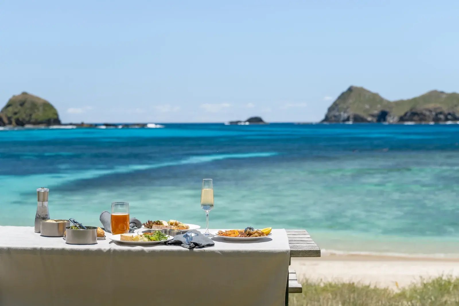 Frokost på bord ved stranden med lagunen bak.