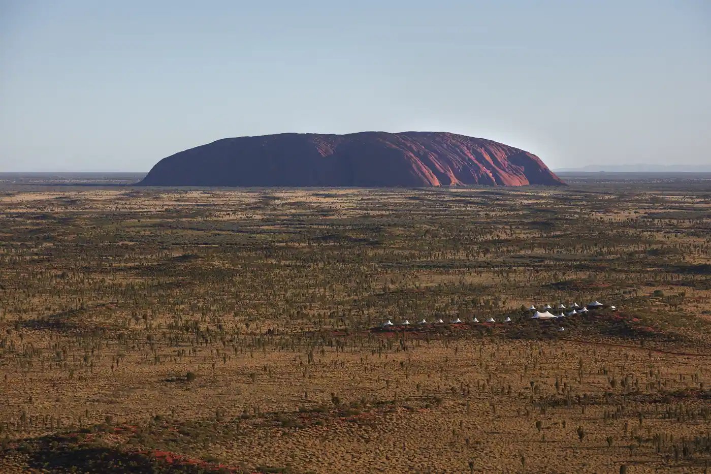 Uluru i horisonten og lodgens telt i det røde landskapet.