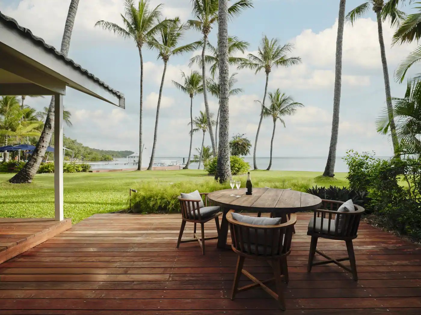 Terrasse med spisebord og palmer foran stranden.