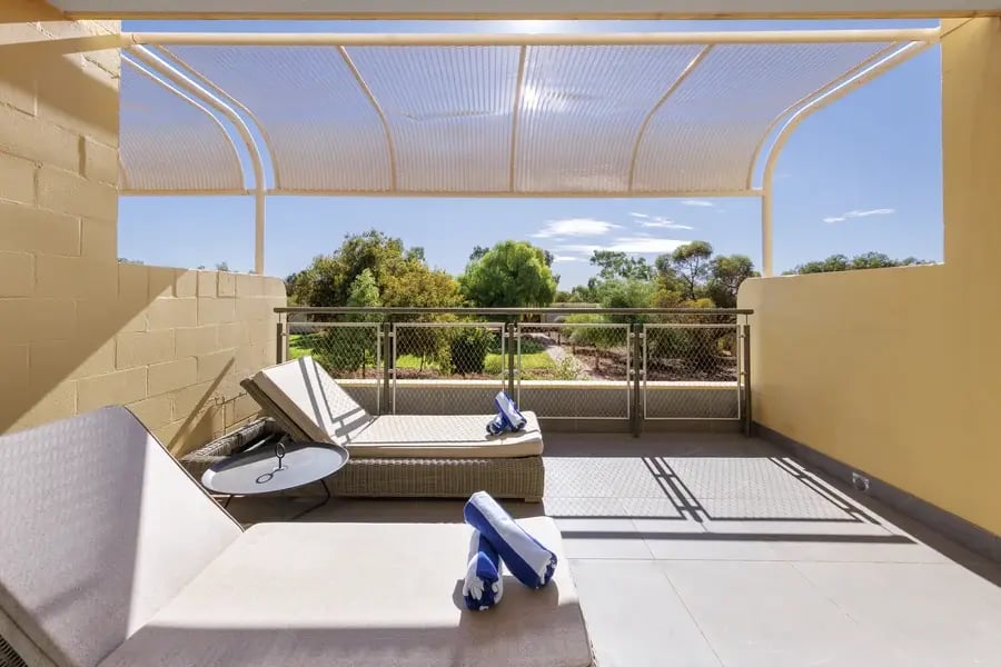 Terrasse med solsenger under et lyst skyggetak.