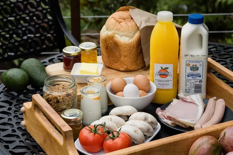 Frokostkurv med brød, juice, egg og frukt på et bord på terrassen.