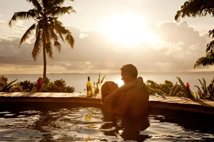 Par i basseng med palmer og solnedgang