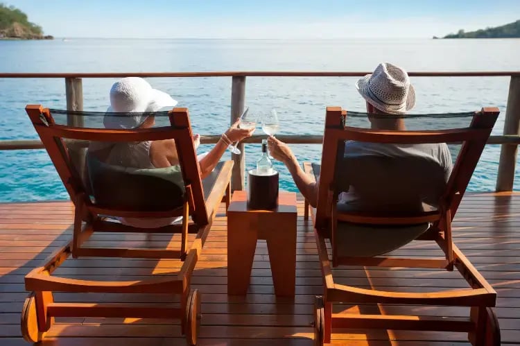 Et par sitter i solsenger med et glass vin og nyter utsikten over havet