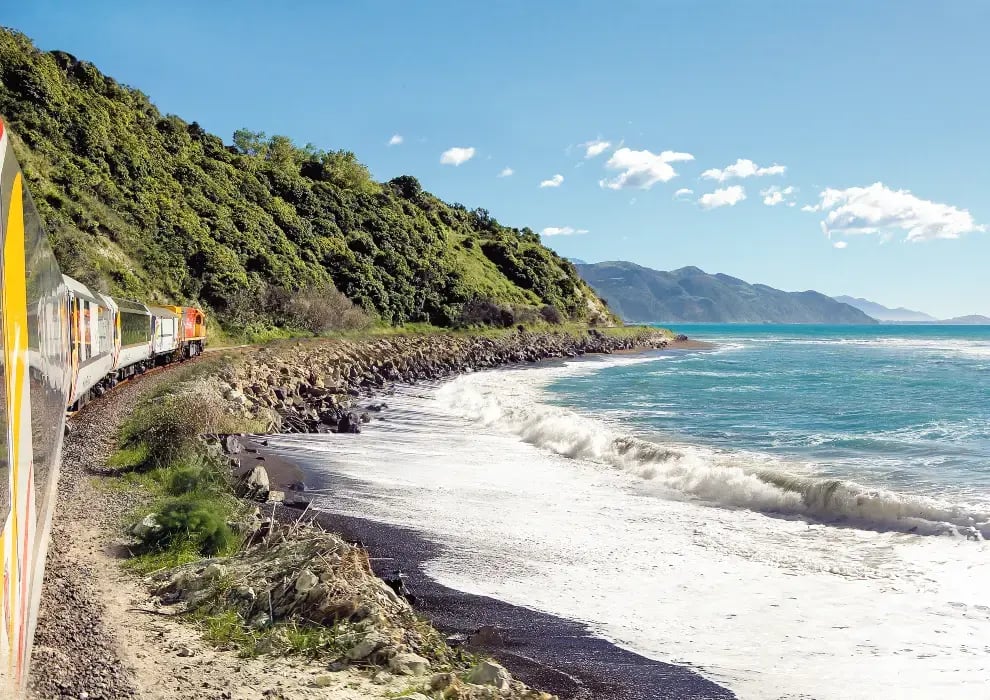 Et tog som kjører langs kysten, mens bølgene slår inn på stranden rett ved.