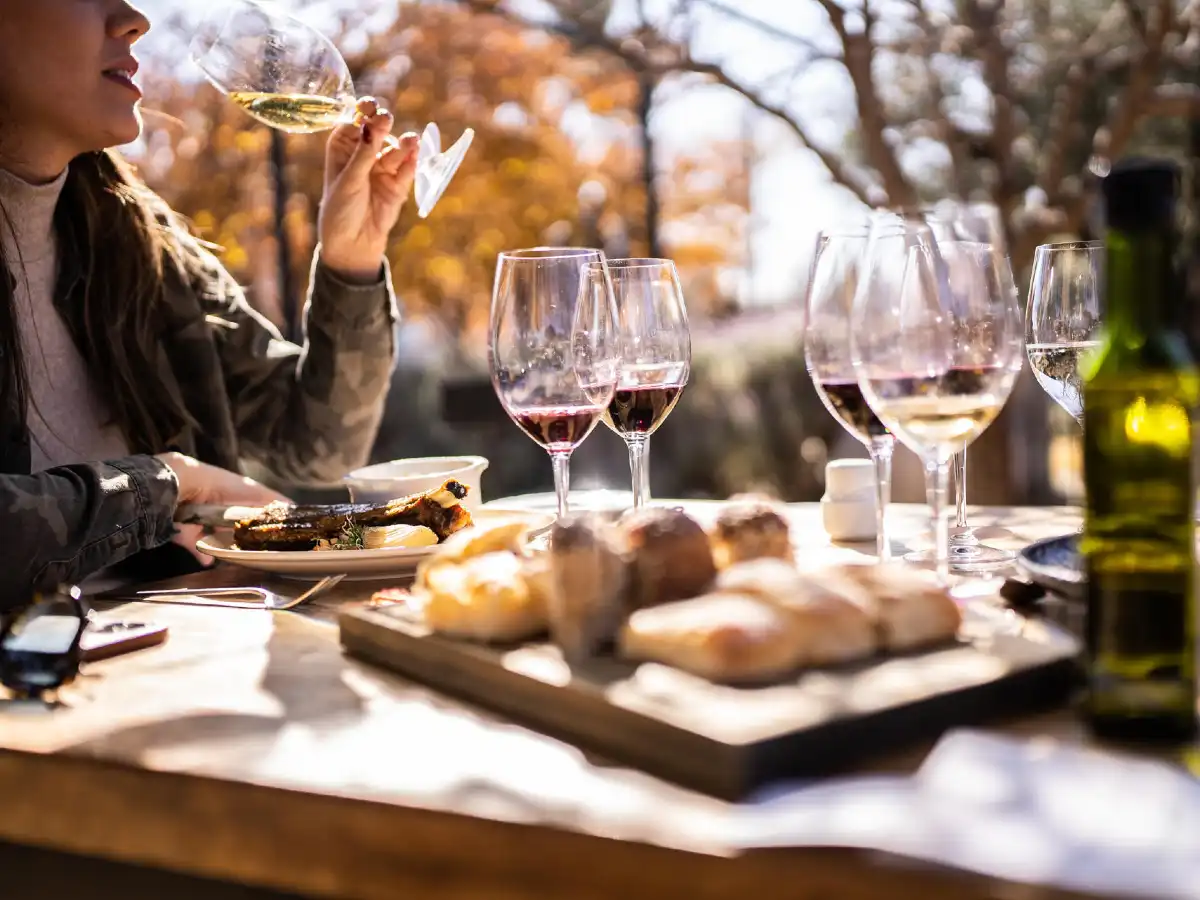 En spisefjøl med mat og vinglass og en hånd som drikker vin fra et glass.