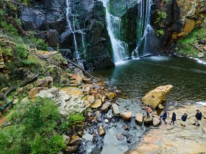Fossefall og vannkulp, med turister som går over steiner. Fossefall og vannkulp, med turister som går over steiner.