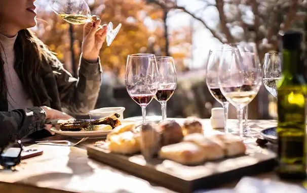 En spisefjøl med mat og vinglass og en hånd som drikker vin fra et glass.